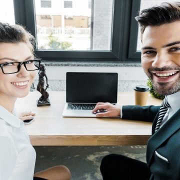 smiling lawyers at workplace with laptop with blank screen and femida in office